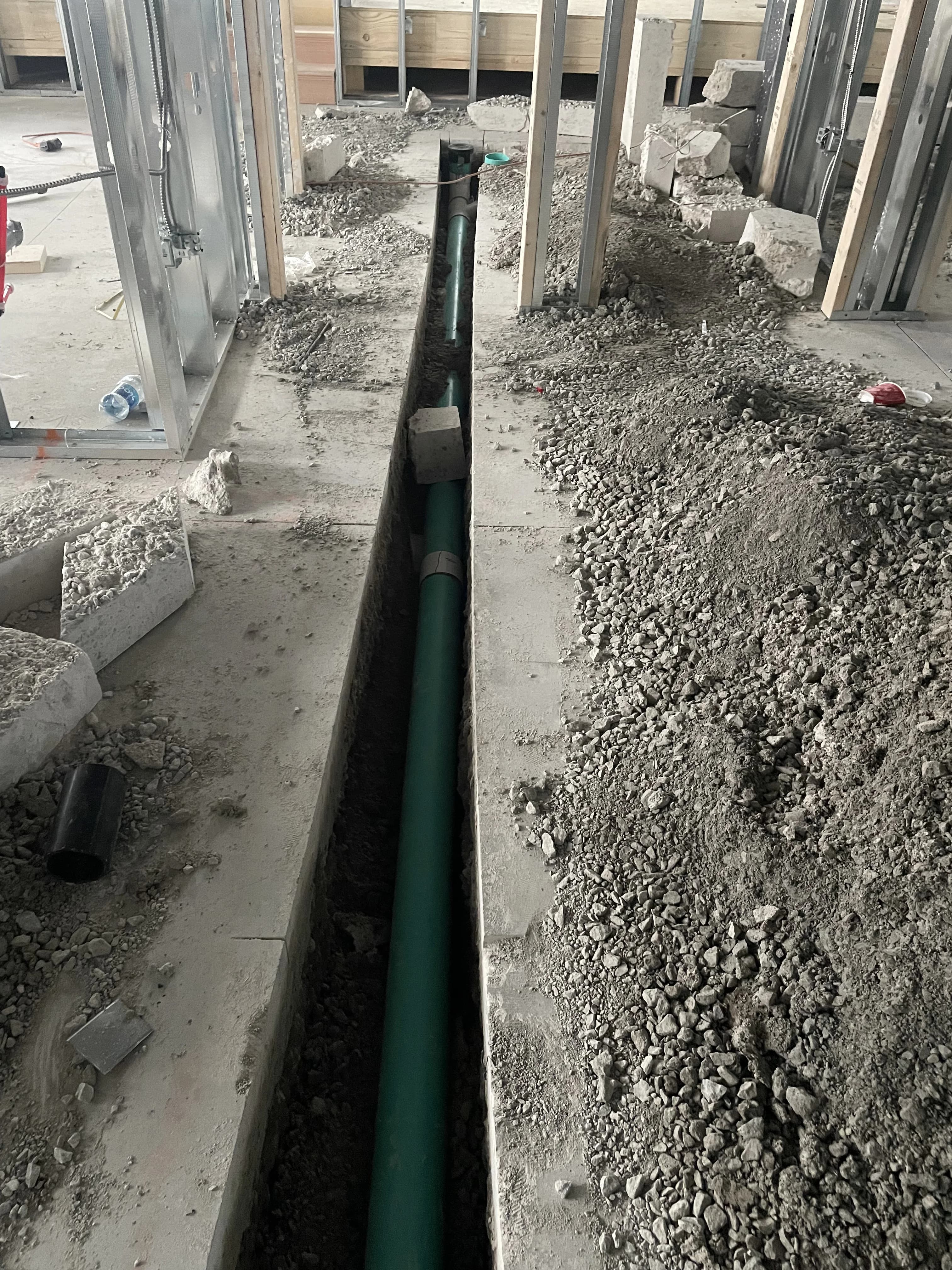 Sewer main trench in Ajax with green PVC laid in a narrow cut through concrete