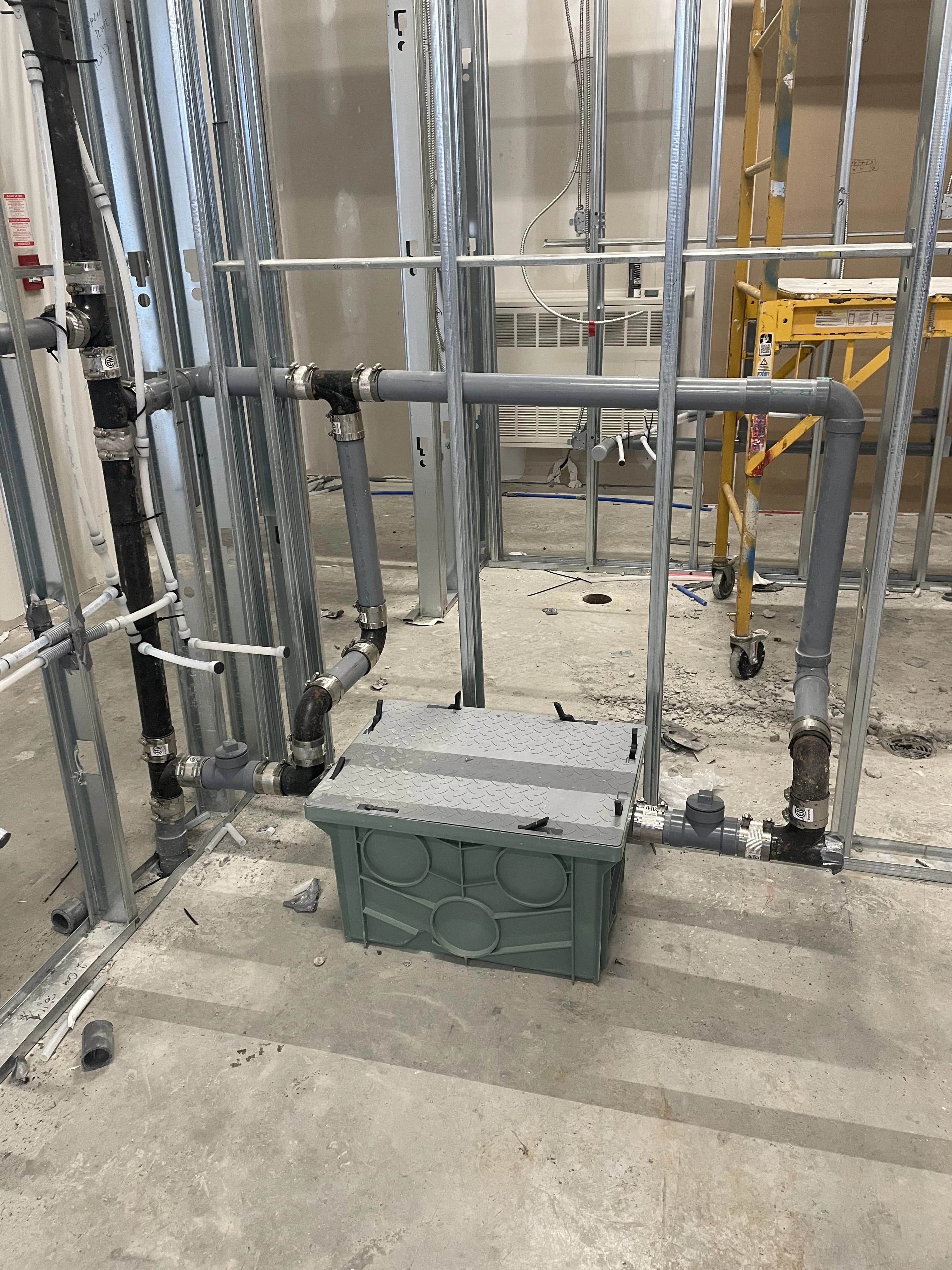 Commercial plumbing rough-in in Ajax with an interceptor unit and drain piping in a framed wall