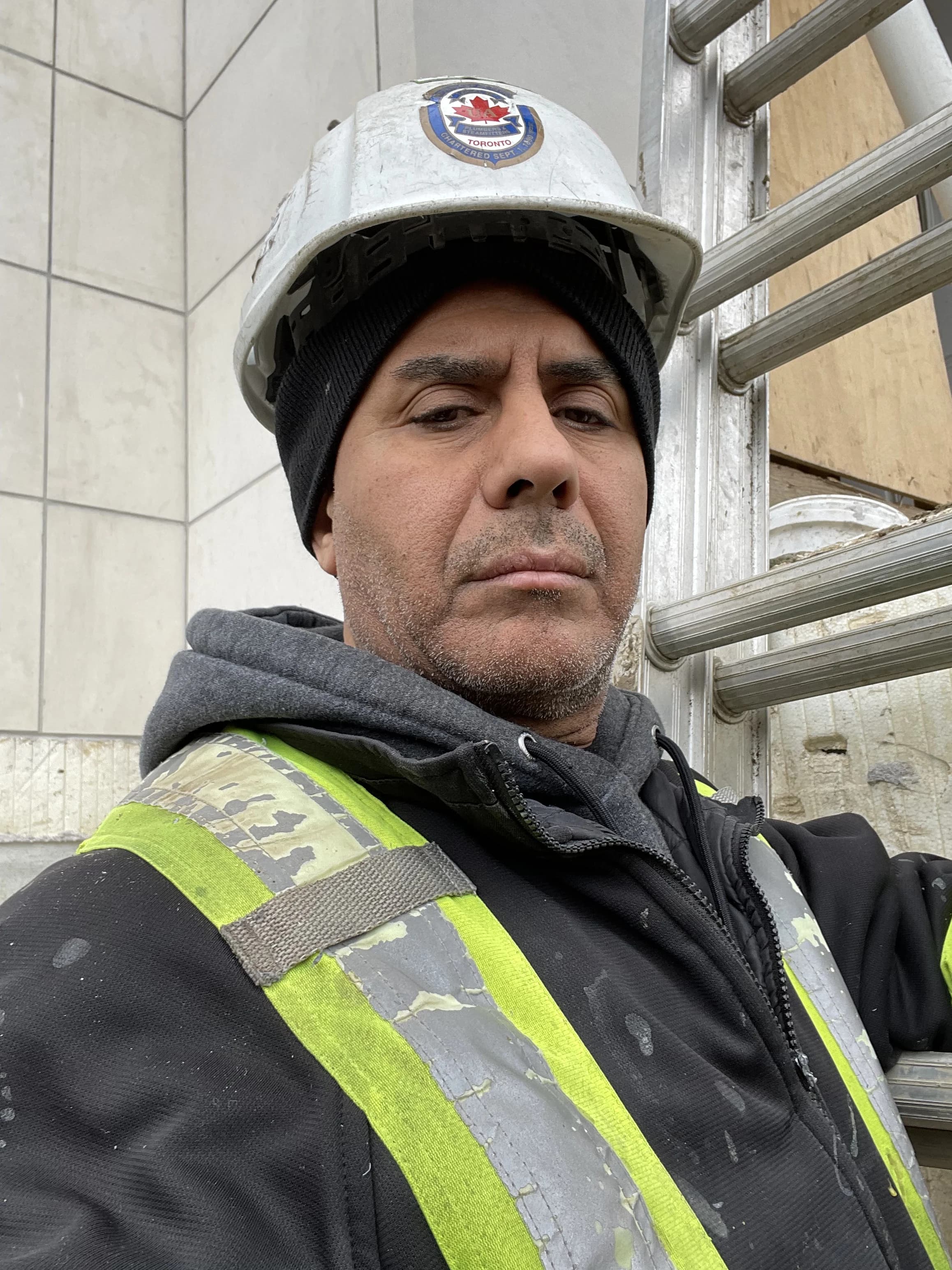 Licensed KK Plumbing technician in hard hat and hi-vis vest on an Ajax job site beside a ladder