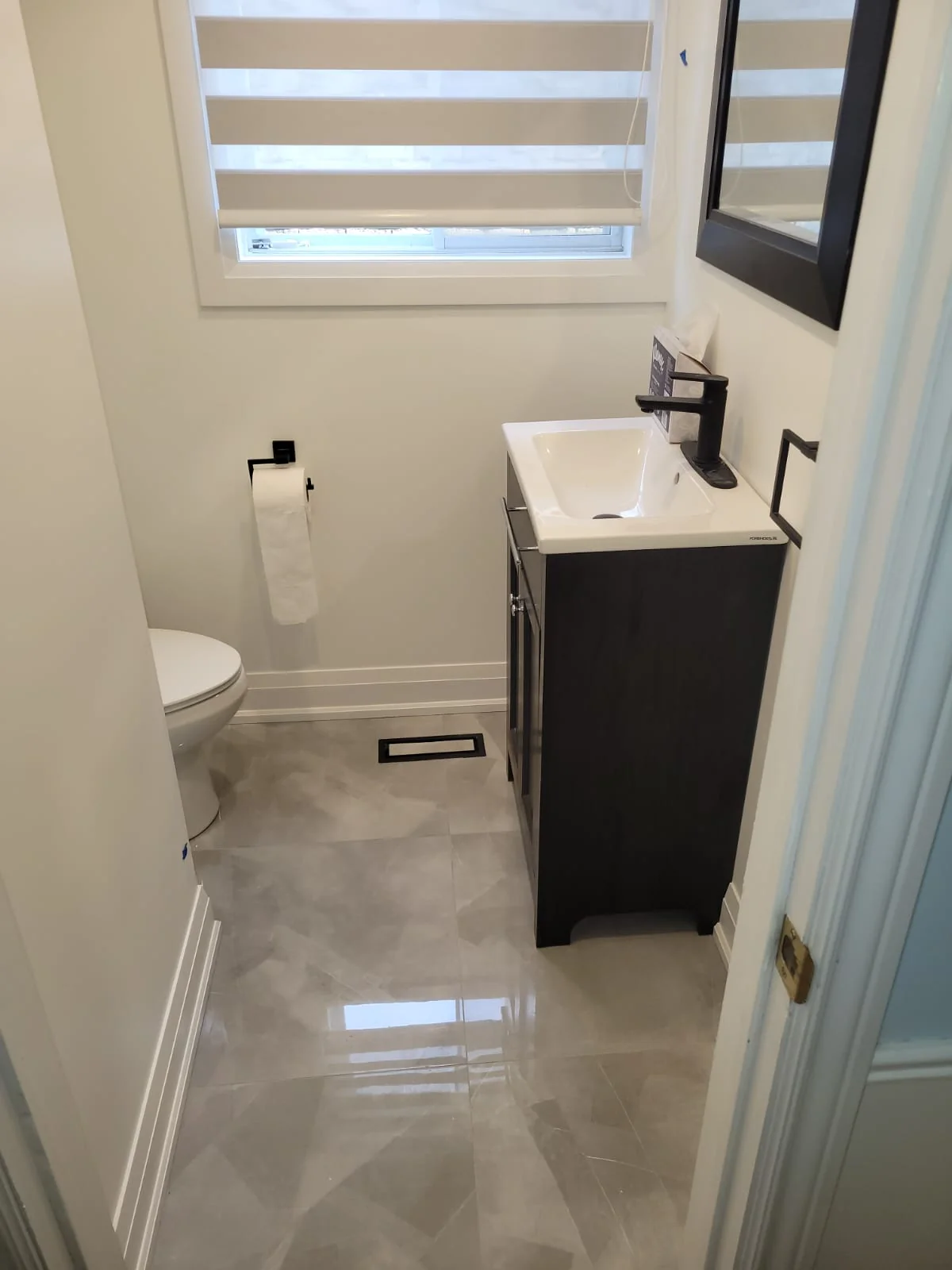 Powder room toilet installation in Ajax with vanity, matte black faucet, and marble-look floor tile